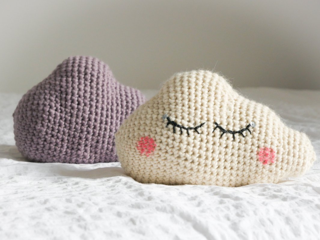 Zwei gehäkelte Wolkenkissen in Creme und Violett auf weißer Decke