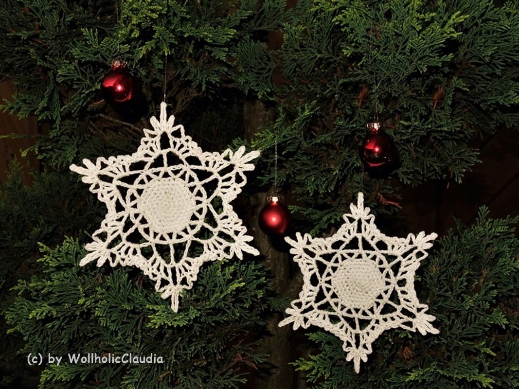 Zwei weiße sternförmige Häkelapplikationen als Dekoration an Nadelbaumzweigen