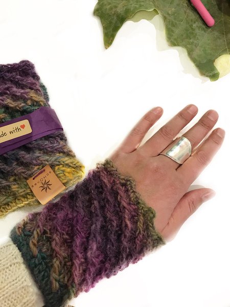 Hand mit gehäkelter, mehrfarbiger, fingerloser Armstulpe