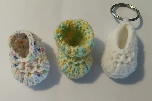 Drei gehäkelte Mini-Babyschuhe, einer mit Metall-Schlüsselring