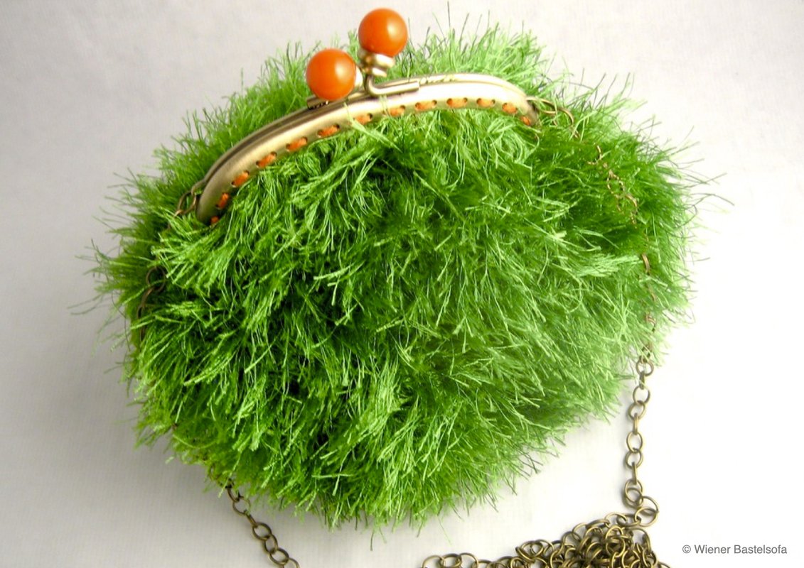 Gehäkelte grüne flauschige Bügeltasche mit Bügelverschluss und Kettenriemen auf hellem Hintergrund.