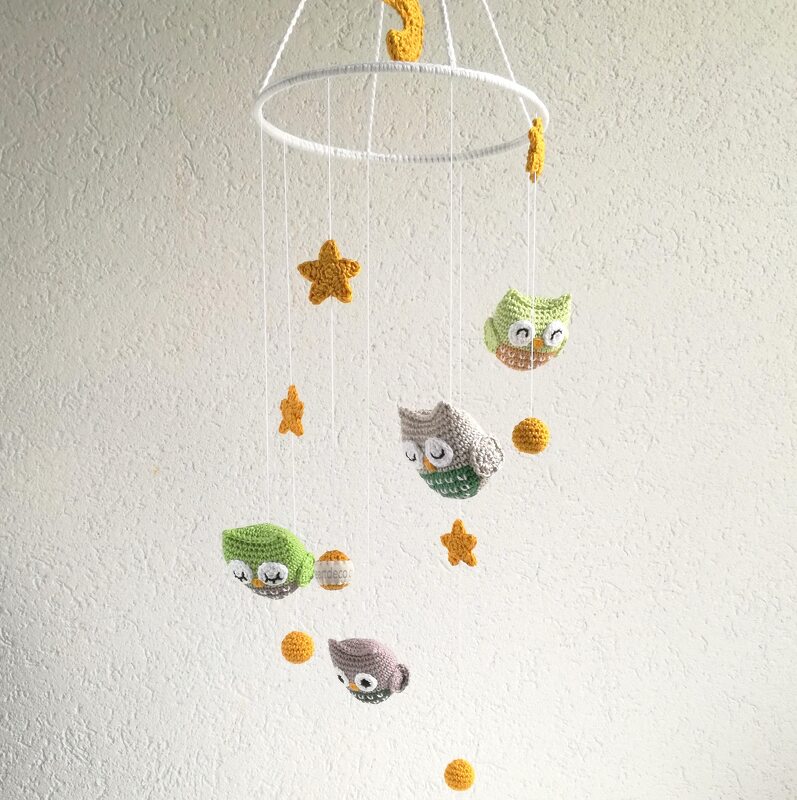 Crochet baby mobile with green, grey, and purple amigurumi owls, yellow stars and small yellow balls hanging from a white hoop.