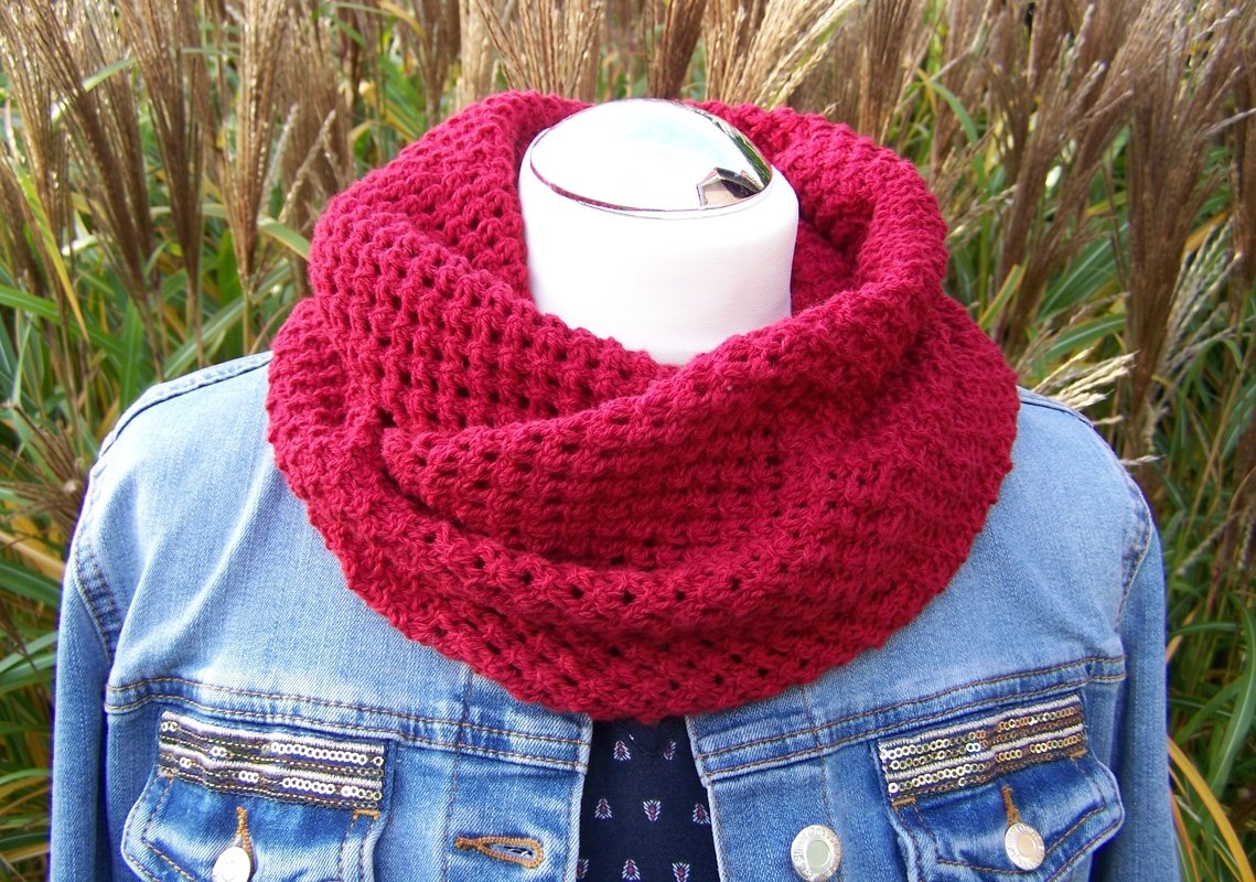 Roter gestrickter Loop mit Lochmuster über einer Jeansjacke auf einer Schaufensterpuppe.