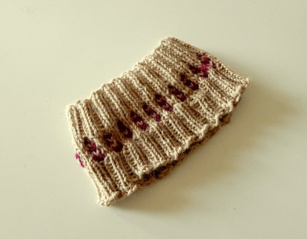 Beige knitted headband with small pink accent stitches on a neutral background.