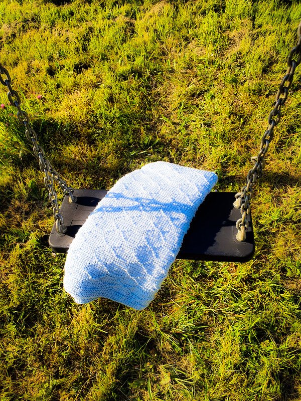 Zarte hellblaue Babydecke gefaltet auf einer Schaukel im sonnigen Gras