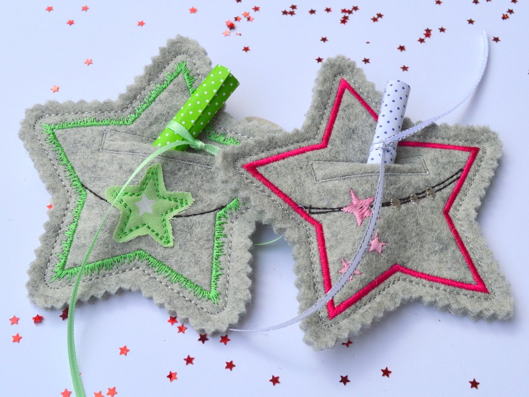 Zwei graue Filzsterne mit grüner und pinker Stickkante, jeweils mit kleinem Fach, Bändern und Sternkonfetti