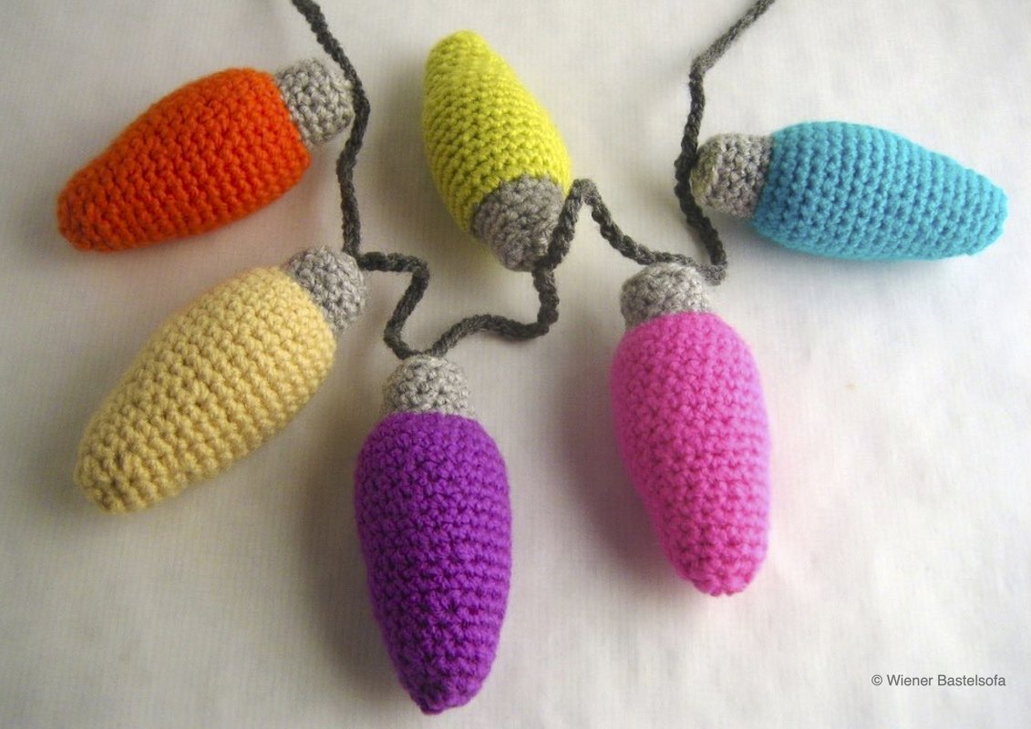 Gehäkelte Lichterkette mit sechs bunten Glühbirnen (Orange, Gelb, Limettengrün, Lila, Pink, Hellblau) auf hellem Hintergrund.