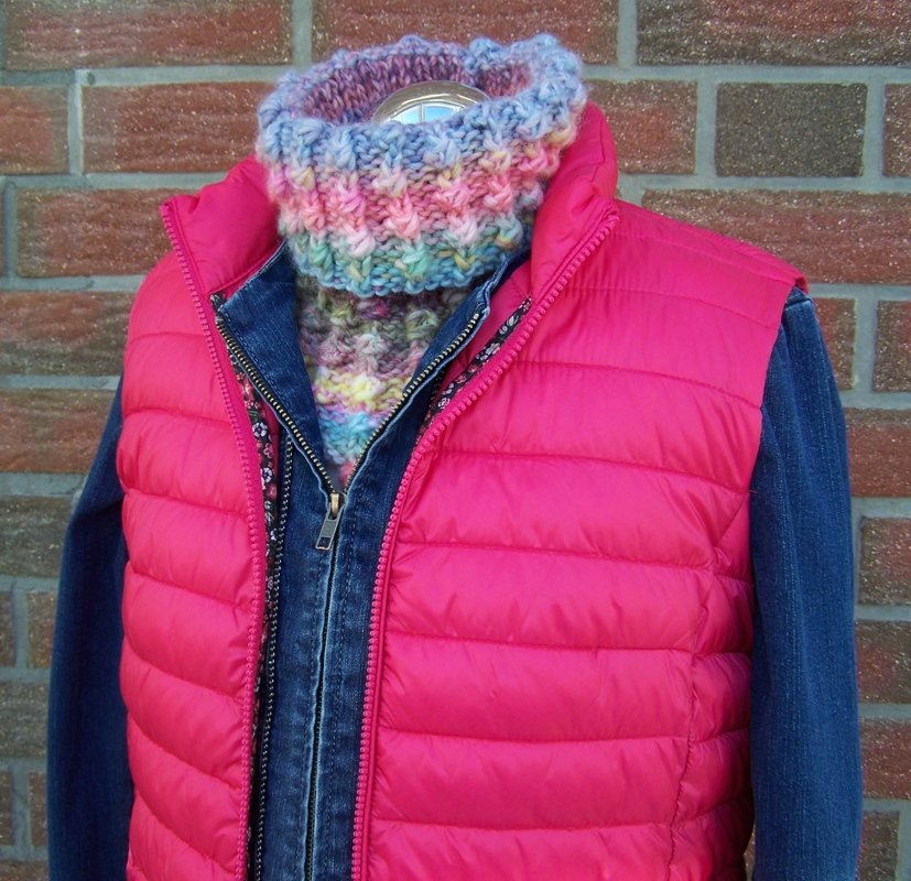 Gestrickter Kragenschal in Pastelltönen unter pinker Steppweste und Jeansjacke.