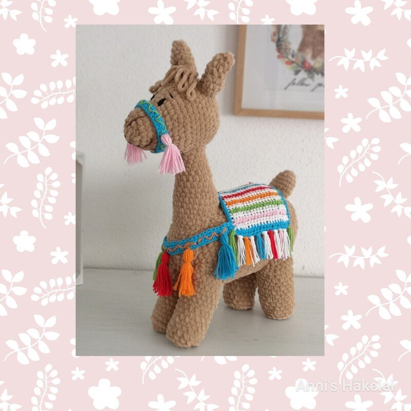 Beiges Amigurumi-Lama mit gestreifter Satteldecke und bunten Quasten