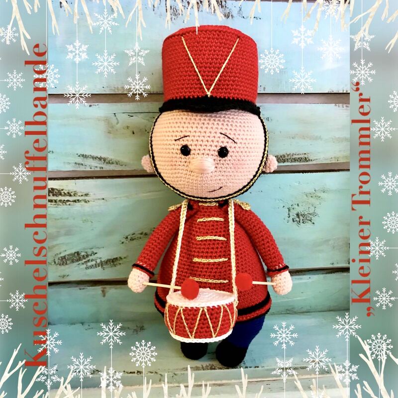 Gehäkelte Amigurumi-Puppe als kleiner Trommler in roter Uniform mit Trommel vor hellem Holzbrett