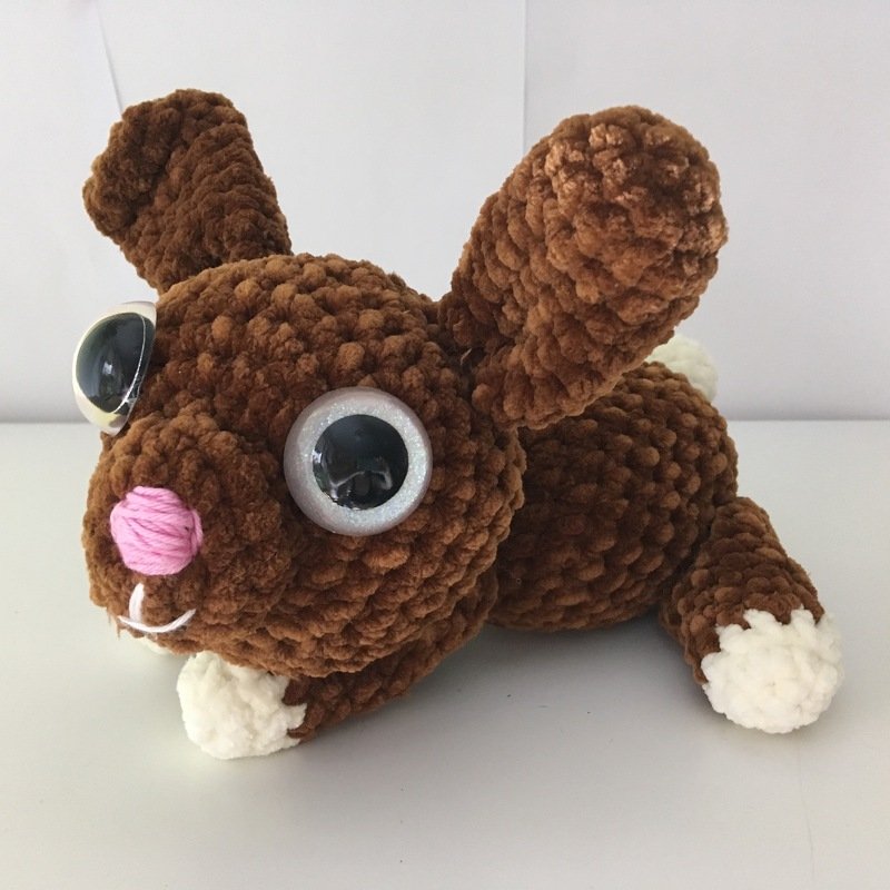 Brauner gehäkelter Amigurumi-Hase mit großen Wackelaugen, rosa Nase und weißen Pfoten.