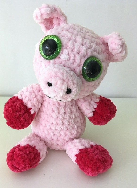 Gehäkeltes rosa Amigurumi‑Schwein mit großen grünen Glitzeraugen und roten Pfoten