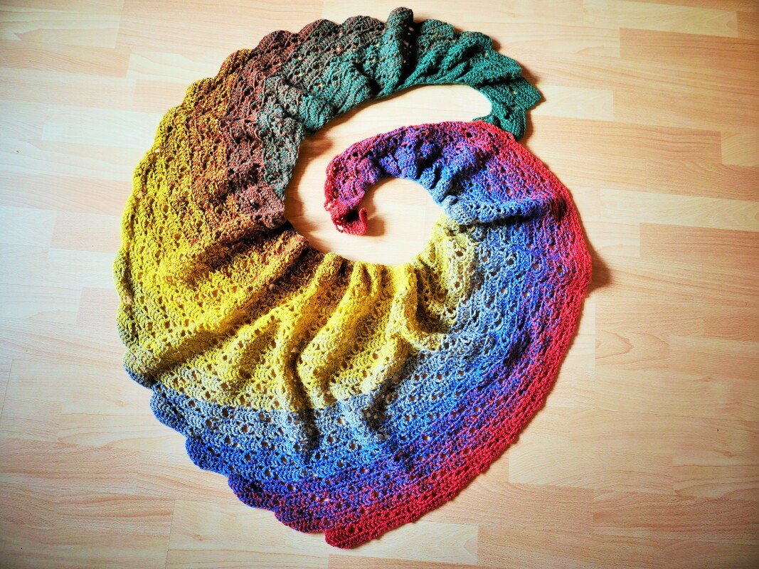 Gehäkeltes Spiraltuch mit Farbverlauf von Grün bis Rot und feinem durchbrochenem Lochmuster auf hellem Holzboden.