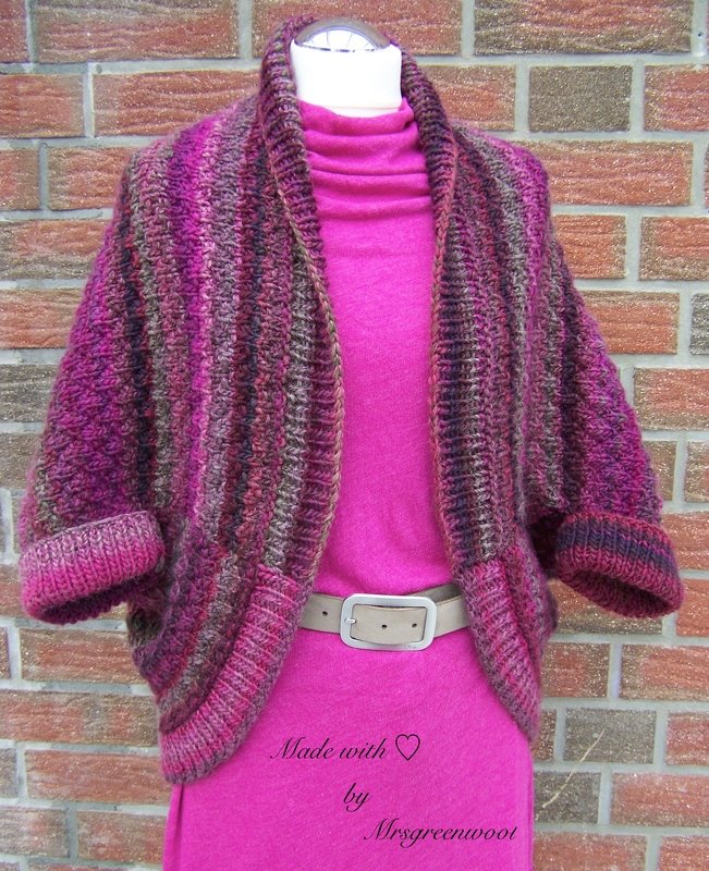 Gestrickter kurzgeschnittener Seelenwärmer in Pink- und Beerenstreifen auf Schaufensterpuppe vor Backsteinwand