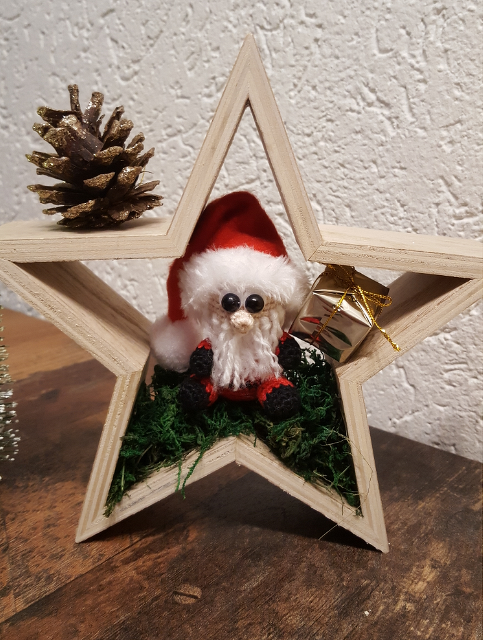 Gehäkelter Weihnachtsmann-Amigurumi in Holzstern mit Moos, Geschenk und Tannenzapfen als DIY-Dekorationsidee