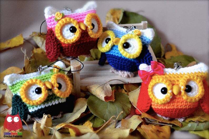 Four colorful crocheted owl keychains with large eyes and beaks, displayed on autumn leaves.