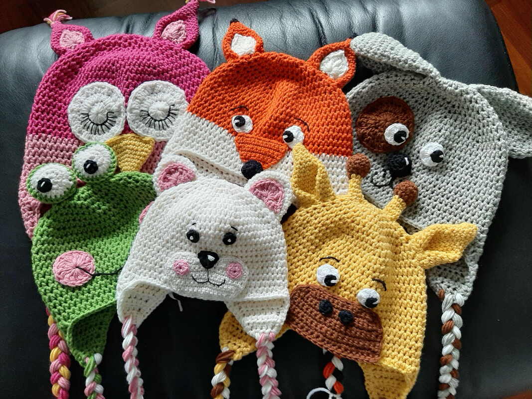 Sechs gehäkelte Tiermützen mit Ohren und geflochtenen Bändern (Eule, Frosch, Fuchs, Elefant, Bär, Giraffe)
