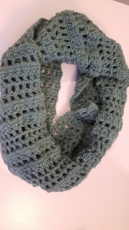 Blue-green crocheted cowl with open lacy stitch pattern.