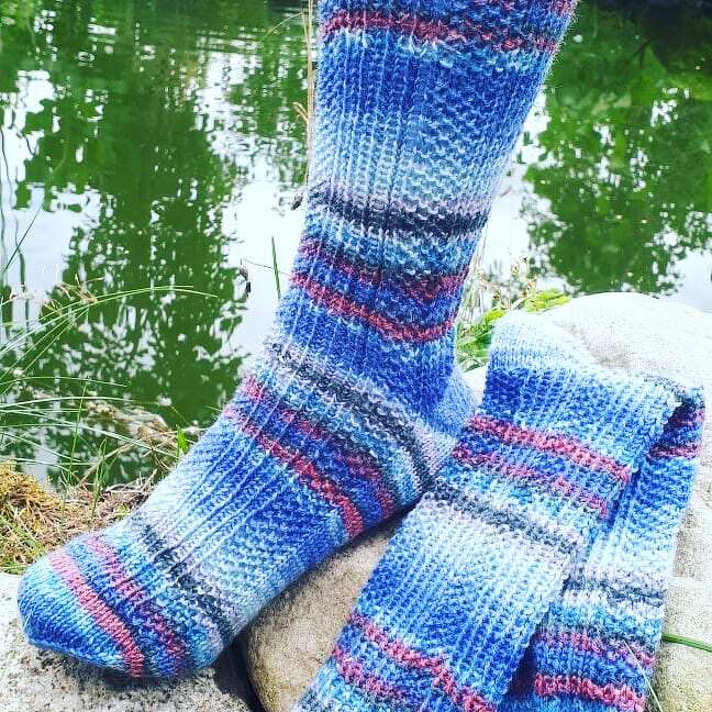 Blau melierte handgestrickte Herrensocken auf einem Stein am Teich