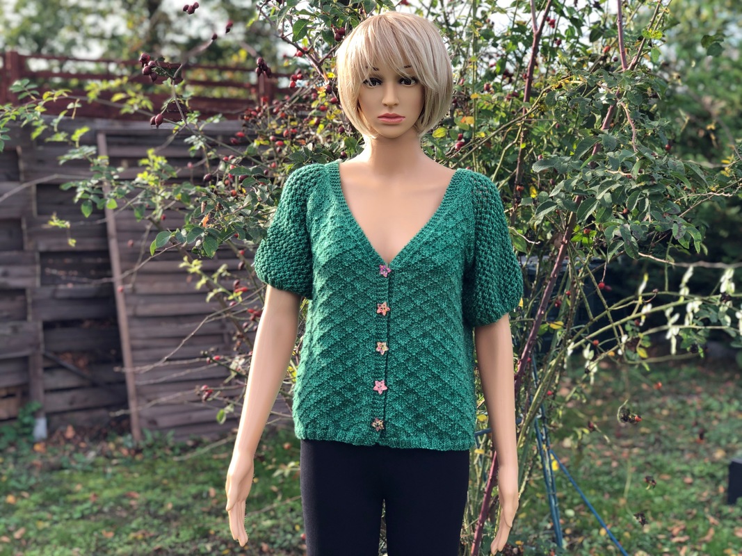 Schaufensterpuppe mit grünem, gestricktem Cardigan mit kurzen Puffärmeln und sternförmigen Knöpfen
