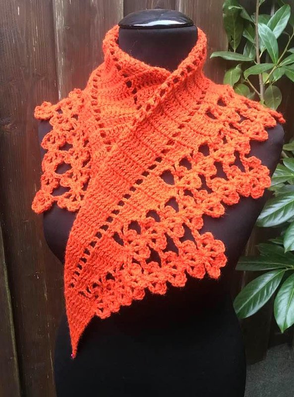 Gehäkeltes orangefarbenes Dreieckstuch mit blütenförmiger Spitzenkante auf schwarzer Schaufensterpuppe