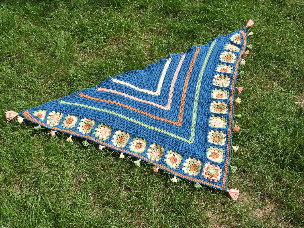Gehäkeltes blaues Dreieckstuch mit Streifen, Granny Squares und Quasten auf Rasen