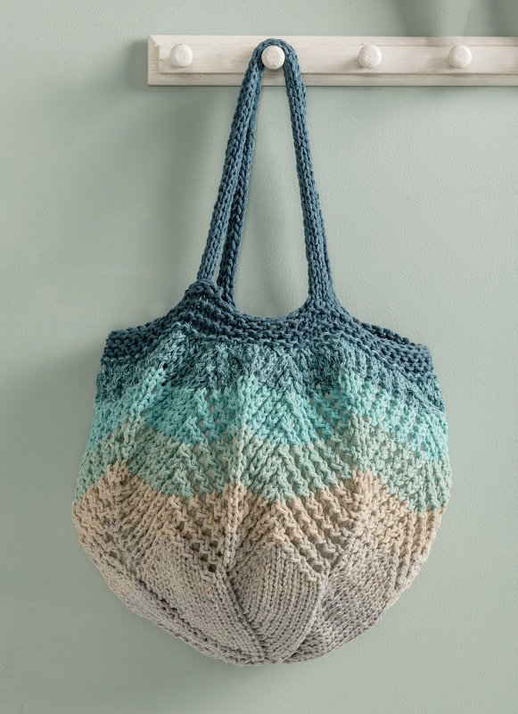 Gestrickte Tasche in Blautönen, Türkis und Beige mit Chevron-Muster an einer Hakenleiste hängend.
