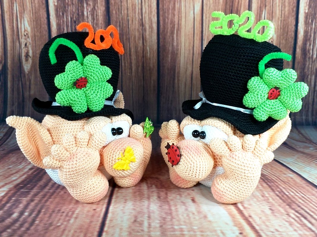 Close-up of two crocheted amigurumi heads showing stitch detail, ear shaping, and top hats with green clovers and insect embellishments