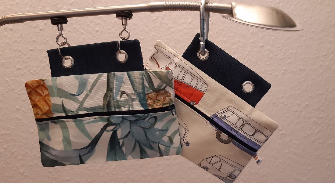 Vier Utensilo-Taschen aus Stoff mit Ananas- und Campingbus-Mustern an Ösen hängend