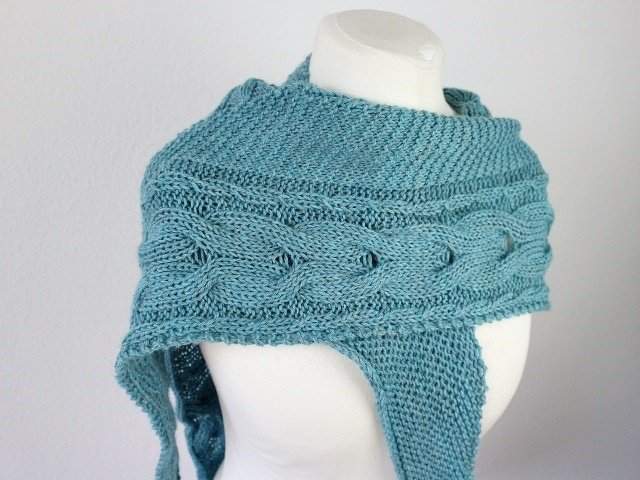 Teal knitted triangle shawl with cable band draped on a mannequin