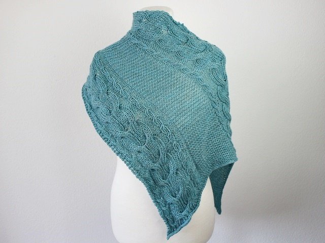 Teal knitted triangle shawl with cable patterns on a white dress form.