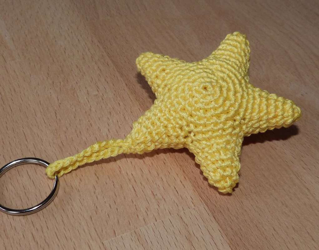 Gehäkelter gelber Stern-Schlüsselanhänger auf Holzuntergrund