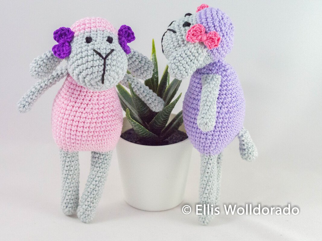 Zwei gehäkelte Amigurumi‑Schäfchen, eines rosa und eines lila, mit Schleifen neben einer kleinen Sukkulente
