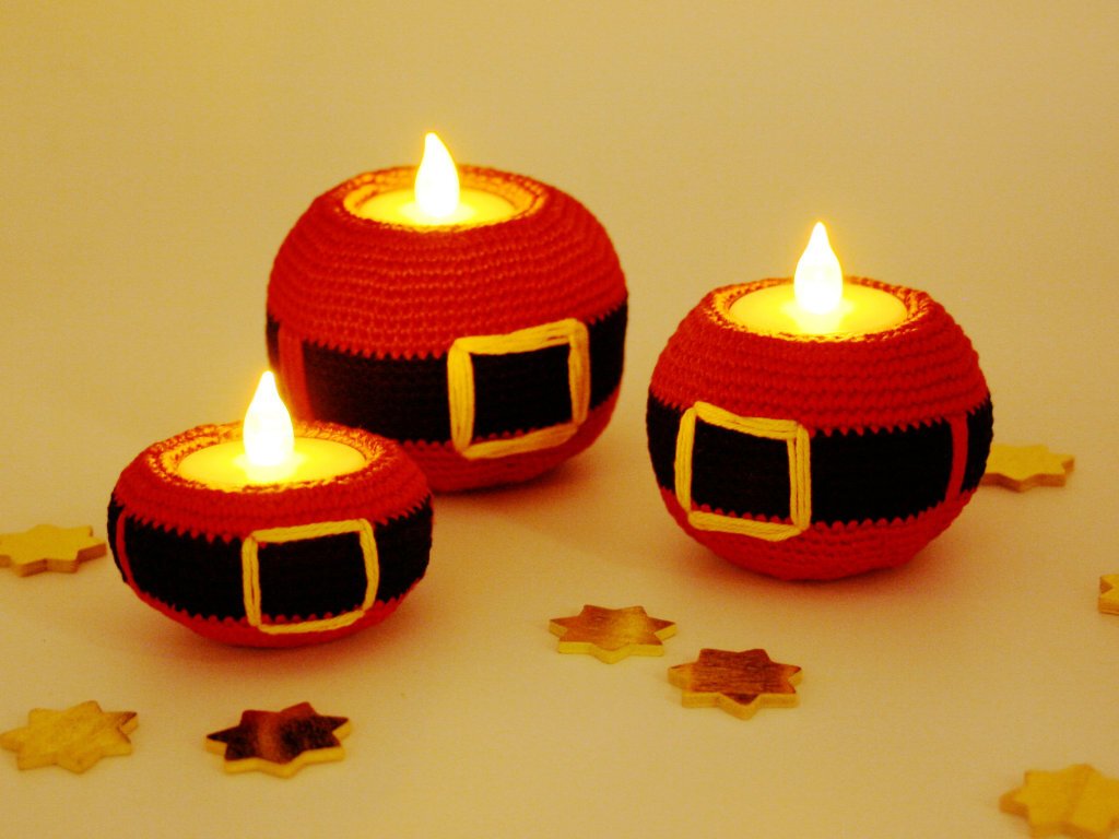 Three red crocheted Santa belt candle holders with glowing LED lights and scattered wooden star cutouts on a light surface.