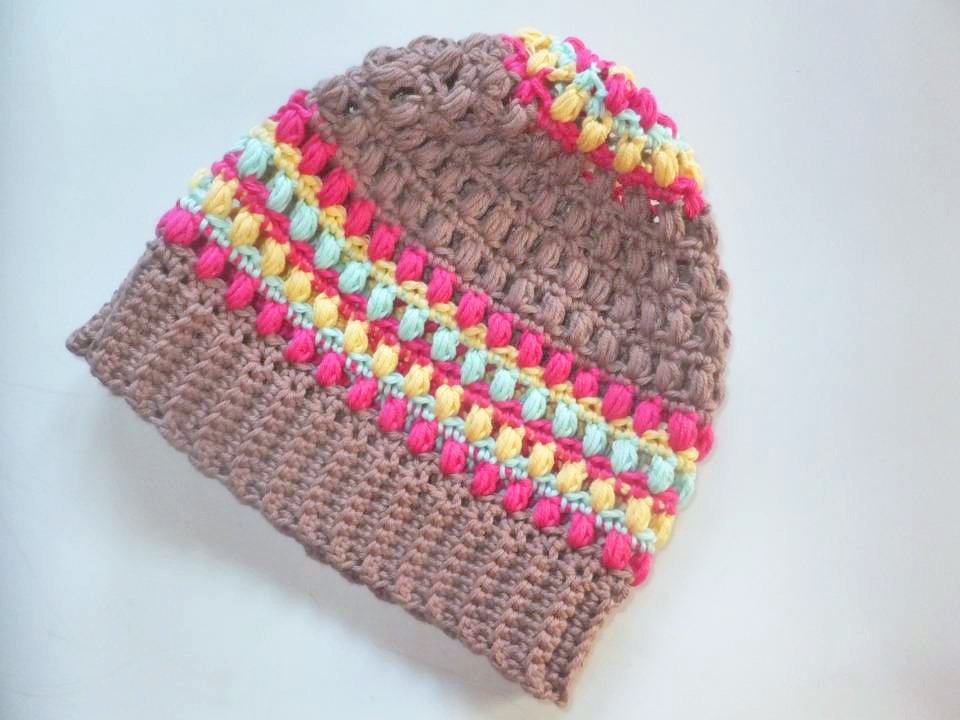 Gehäkelte beige Beanie mit pinken, gelben und mintfarbenen Puffstreifen auf hellem Hintergrund