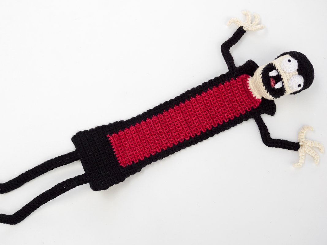 Black and red crocheted vampire bookmark with cream face, white eyes and small fangs on a white background.