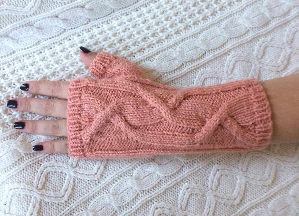 Rosa gestrickte fingerlose Armstulpe mit Zopfmuster auf hellem Strickhintergrund