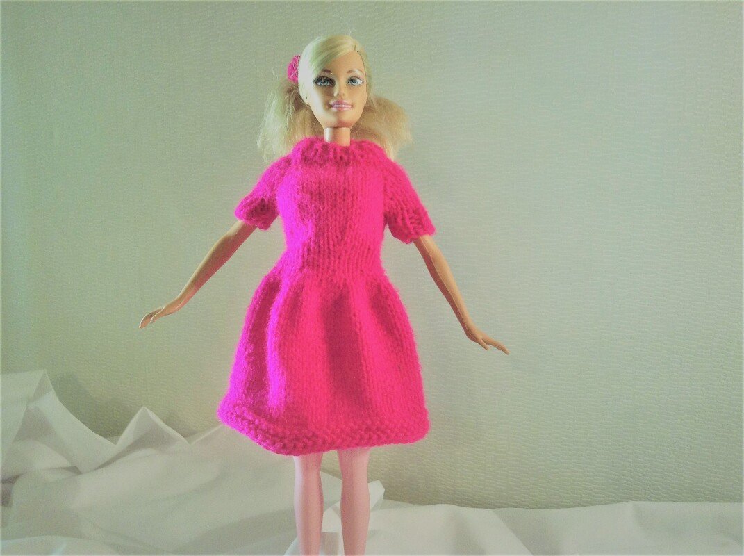 Blonde Puppe trägt ein leuchtend pinkes, kurzärmeliges Strickkleid