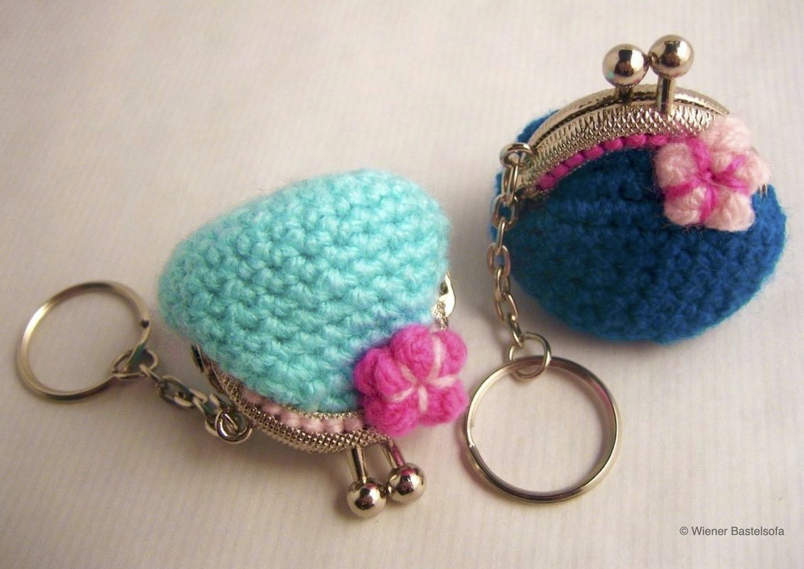 Zwei gehäkelte runde Münztäschchen als Schlüsselanhänger, helltürkis und dunkelblau, mit Metallbügel und rosa Blüten
