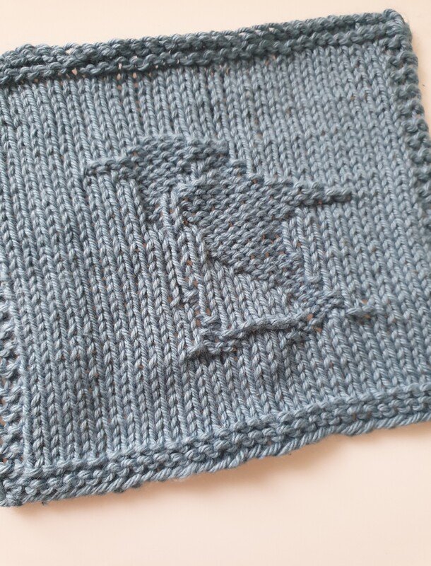 Blue knitted swatch with garter border and raised textured motif