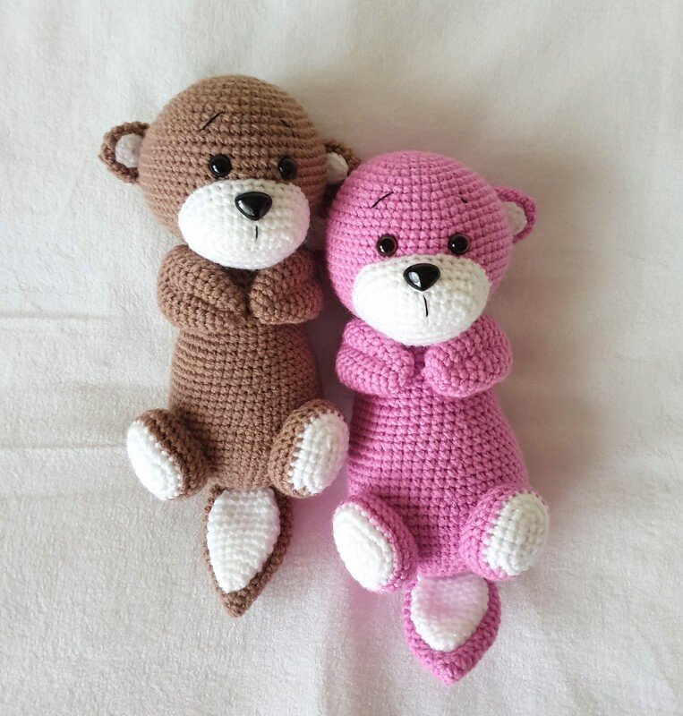 Zwei schlanke gehäkelte Amigurumi-Tiere in Braun und Rosa mit weißen Pfoten und kurzem Schwanz