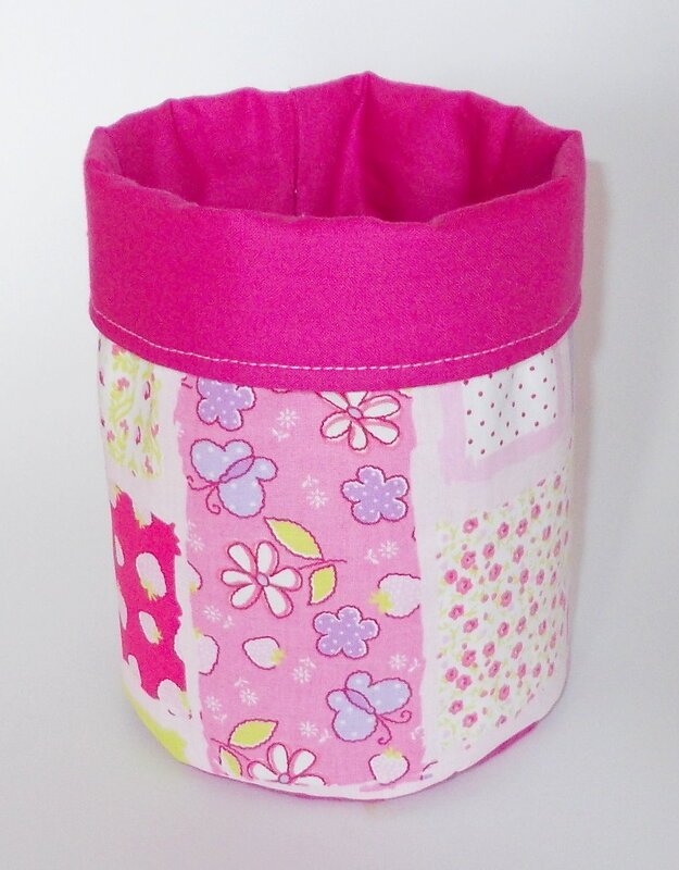 Rosa-weißes Stoffkörbchen mit Patchwork aus Blumen und Schmetterlingen vor weißem Hintergrund.