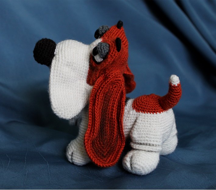 Gehäkelter Basset Hound Amigurumi mit langen roten Schlappohren auf blauem Hintergrund