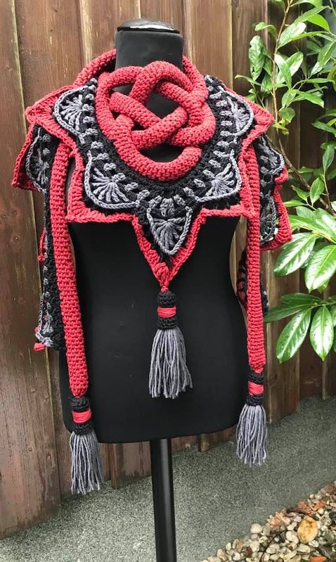 Rotes und graues gehäkeltes Dreieckstuch mit geflochtenem Knoten und langen Quasten auf einer Schaufensterpuppe