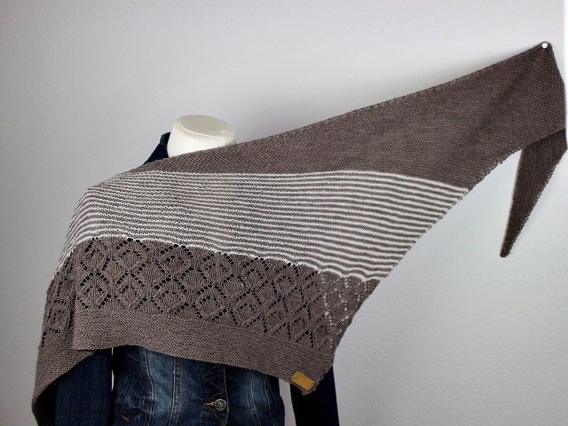 Neutral asymmetrical triangle knitted shawl with cream stripes and scalloped lace edging draped on mannequin
