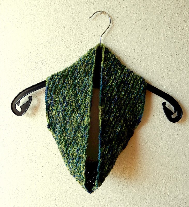 Hand-knitted green and blue variegated cowl on a black hanger