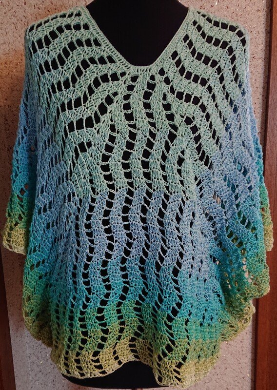 Gehäkelter Damenponcho in Ombre-Farben mit offenem Wellenmuster und V-Ausschnitt auf schwarzer Schaufensterpuppe