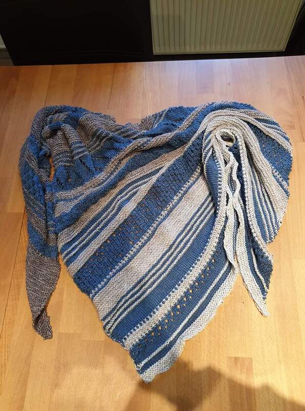Gestricktes Dreieckstuch mit blauen und grauen Streifen und Lochmuster auf Holzboden