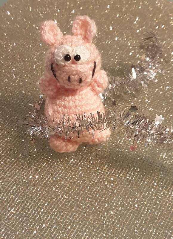 Rosa gehäkeltes Schweinchen mit schwarzen Augenperlen vor silbrig glitzerndem Hintergrund
