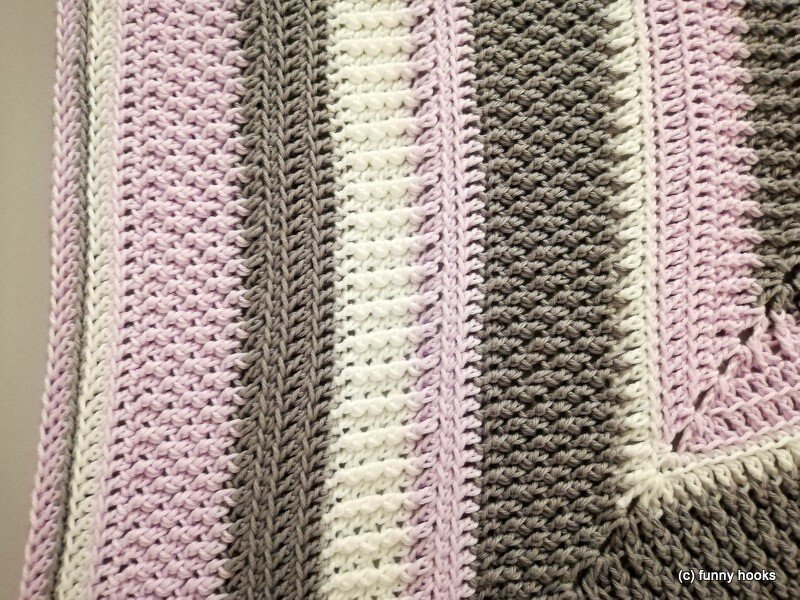 Detailansicht der Maschen und des Rands einer gehäkelten Decke mit Pastellstreifen in Rosa, Grau und Weiß